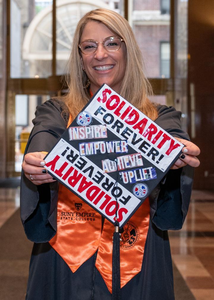 Student standing dressed in graduation robe displaying graduation cap with message that reads solidarity.