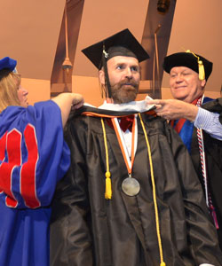 Michael Fletcher Tester, seen here receiving his academic hood for completing his master's, was a student speaker for the 2015 commencement ceremony held on Long Island.